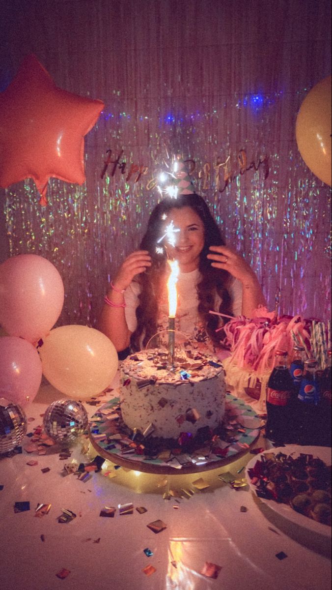 a woman sitting in front of a birthday cake with lit candles on top of it