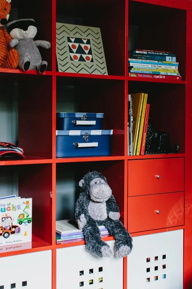 a stuffed animal sitting on top of a red book shelf filled with books and toys