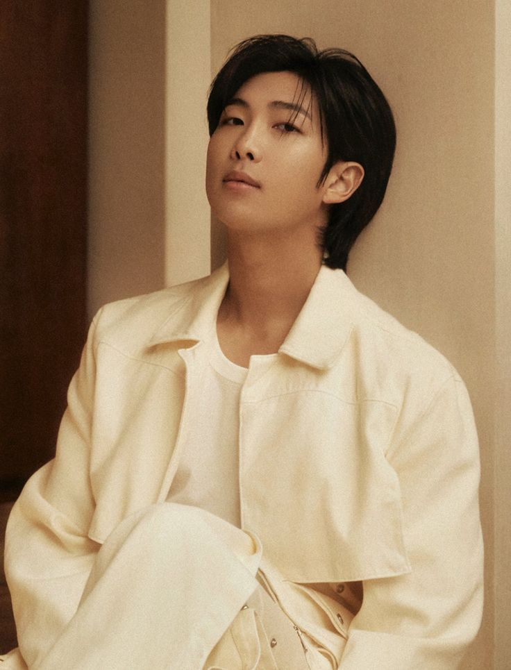 a young man sitting on the floor wearing a white shirt and beige pants with his eyes closed