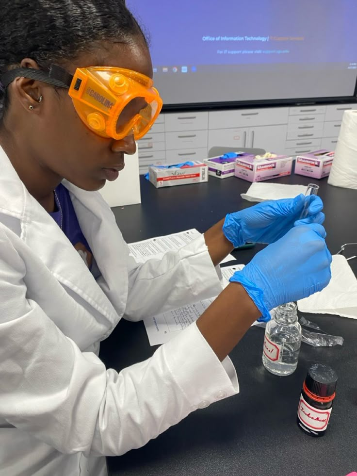 a woman wearing goggles and gloves working in a lab