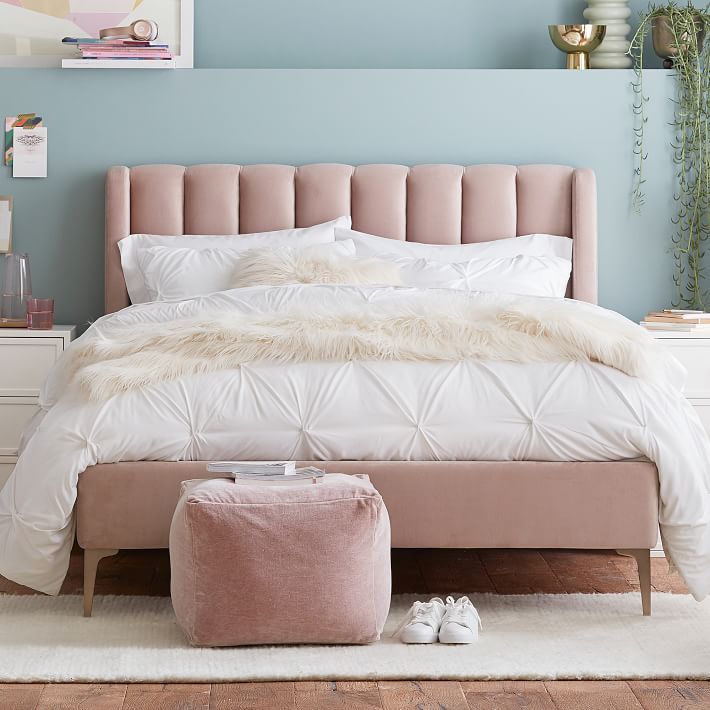 a bedroom with blue walls and white bedding in the center, pink footstool on the floor