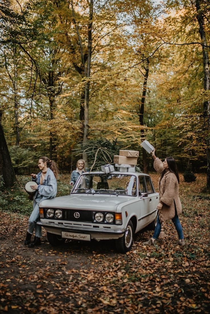 three people standing next to an old car in the woods with their luggage on top