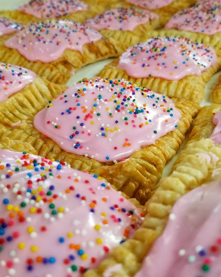 there are many desserts with pink icing and sprinkles on them