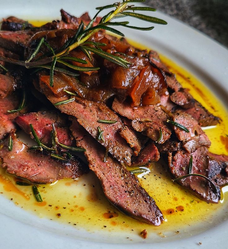 a white plate topped with sliced up meat covered in sauce and garnished with herbs