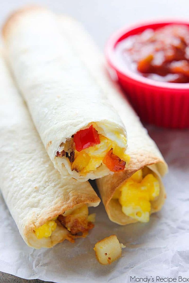 two burritos are sitting next to a bowl of salsa and ketchup