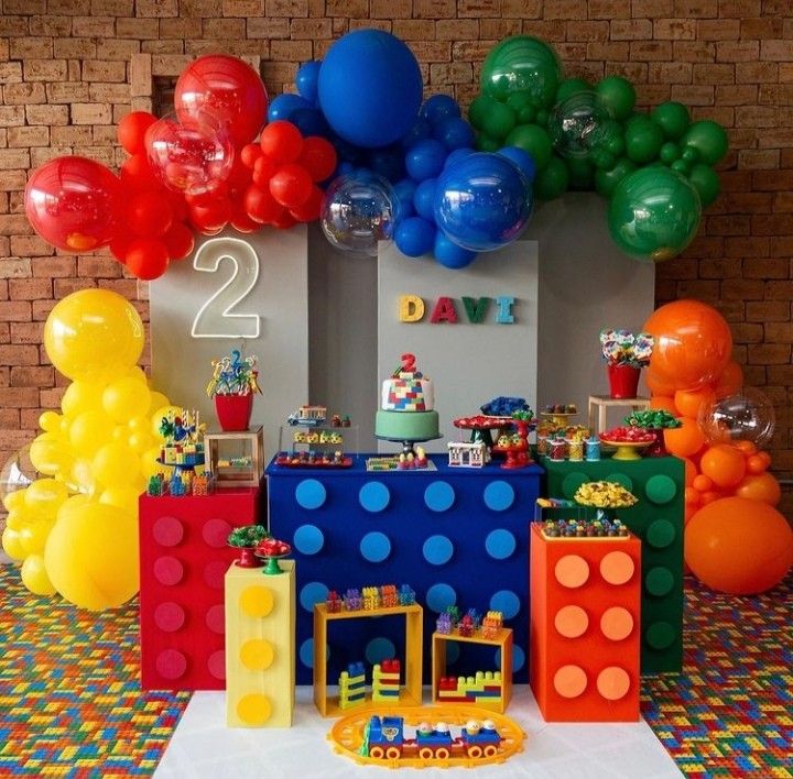 a table topped with lots of balloons next to a wall covered in legos and blocks