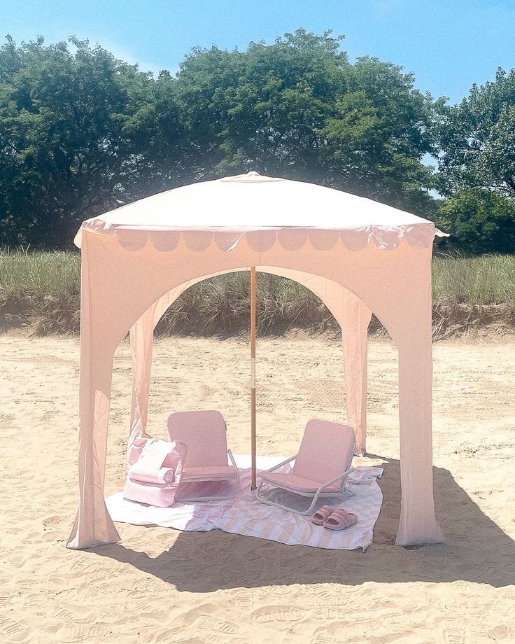 two lawn chairs under a white tent on the sandy beach with trees in the background