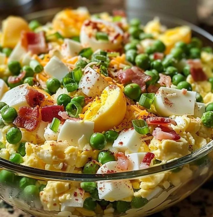 a glass bowl filled with eggs, peas and bacon