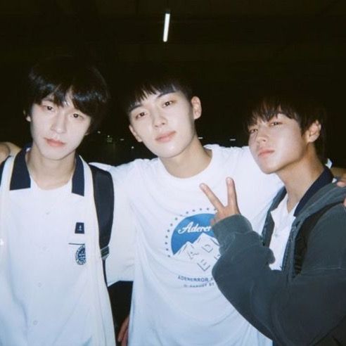 three young men standing next to each other in front of a dark background with one giving the peace sign