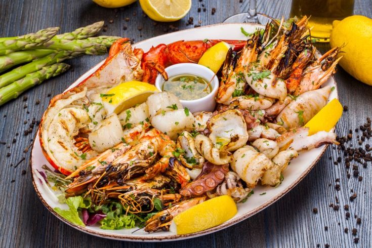 a plate full of shrimp, scallops and asparagus with lemon wedges