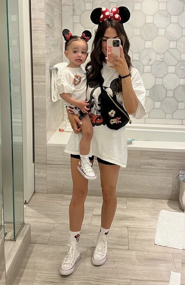 a woman taking a selfie with her child in front of a bathroom mirror wearing minnie mouse ears