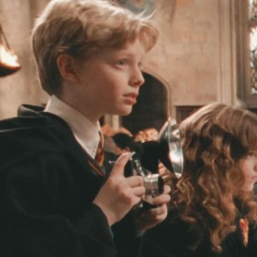 a young boy is holding a camera in front of another child with long curly hair