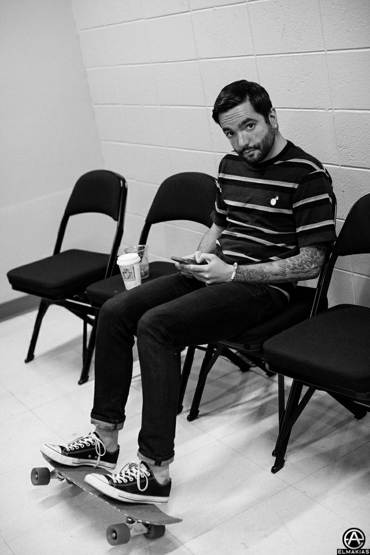 a man sitting in a chair with his feet on a skateboard and holding a drink