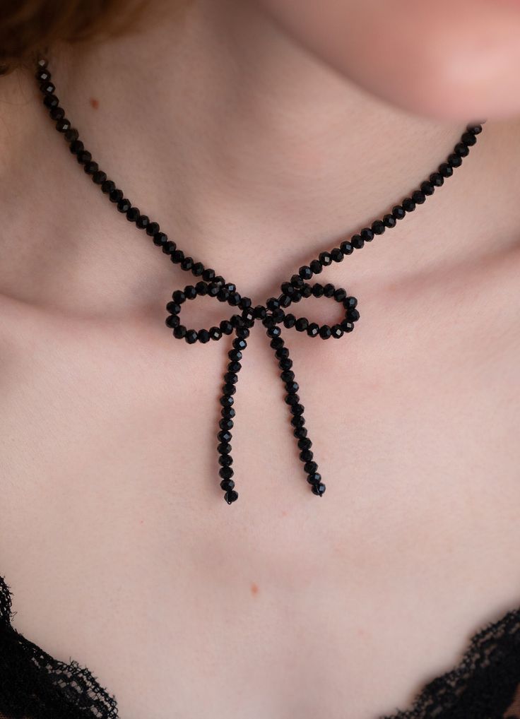 a woman wearing a black beaded necklace with a bow on it's neck