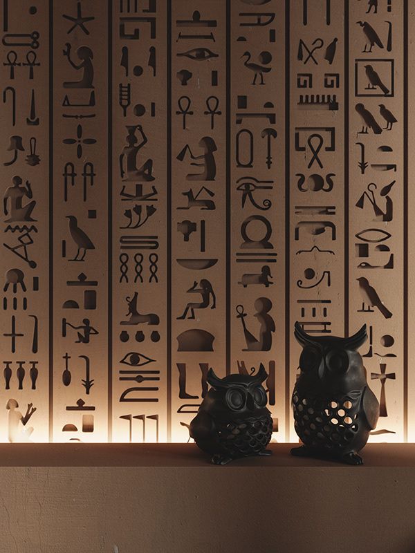 two black owls sitting on top of a shelf in front of egyptian wallpapers