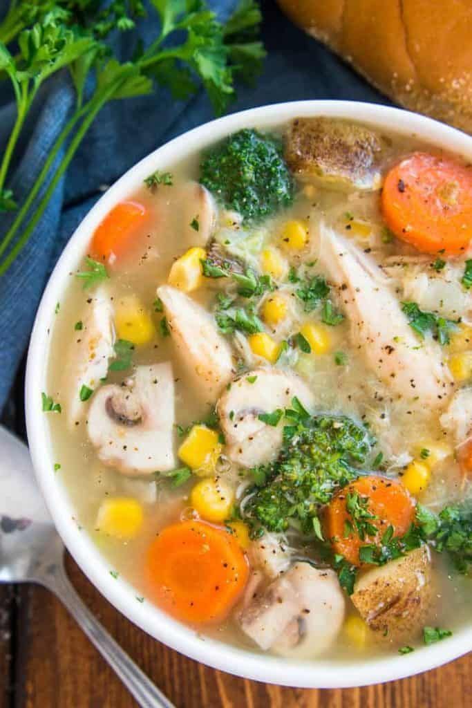 a white bowl filled with chicken, carrots and broccoli next to a loaf of bread