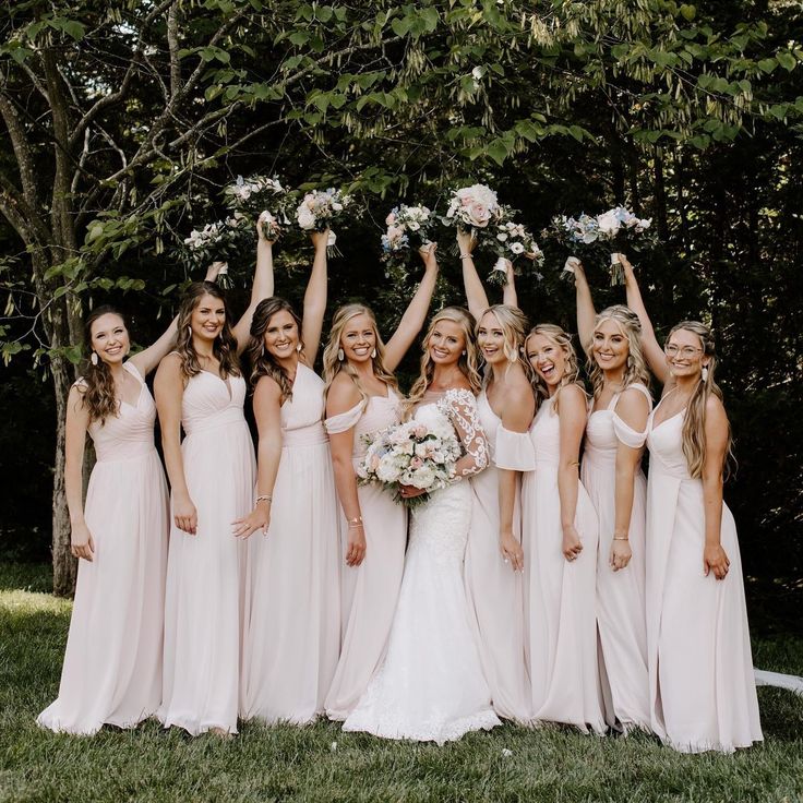 a group of bridesmaids pose for a photo in front of some trees and bushes