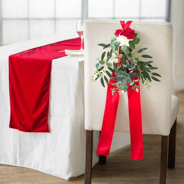 a white chair with a red sash and flower arrangement on it next to a table