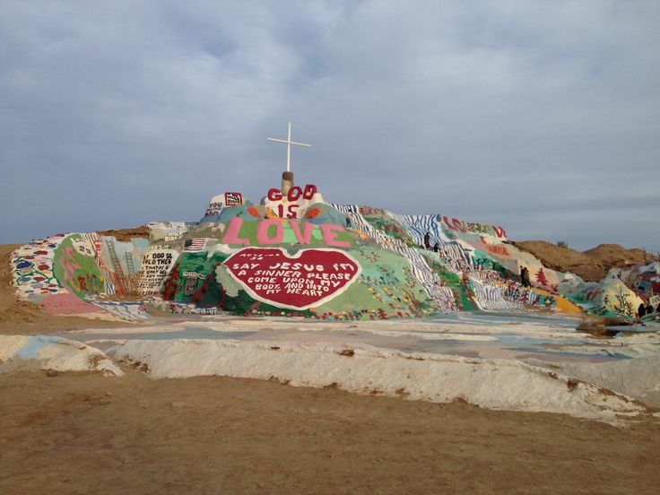 an artisticly decorated hill with a cross on top and graffiti all over the sides