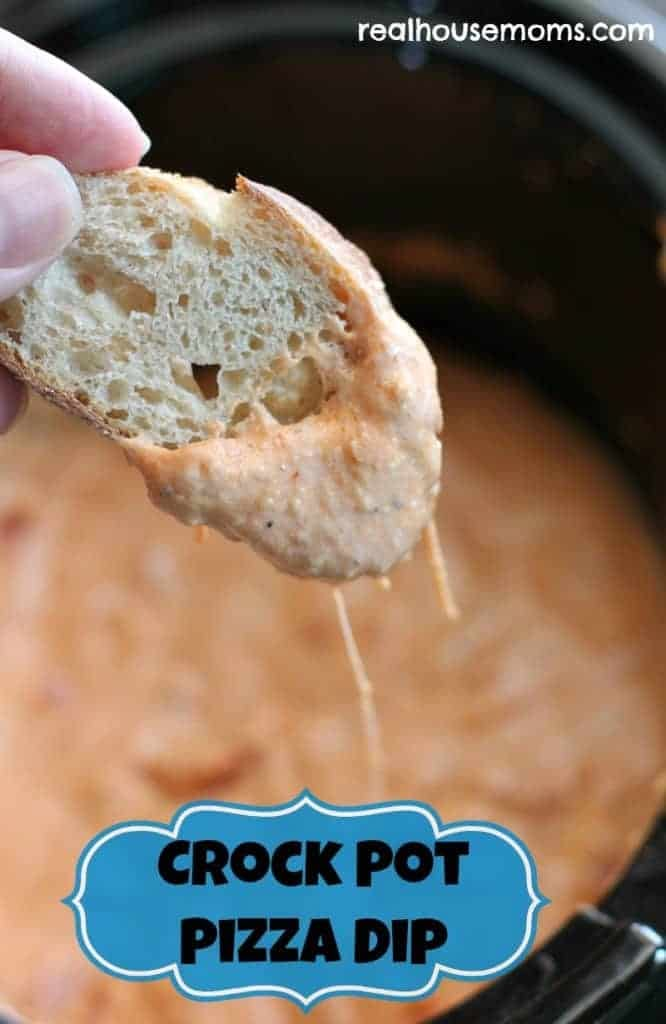 a hand holding a piece of bread over a crock pot pizza dip