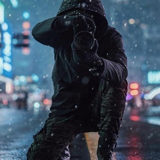 a man standing in the rain taking a photo with his cell phone and wearing a hoodie