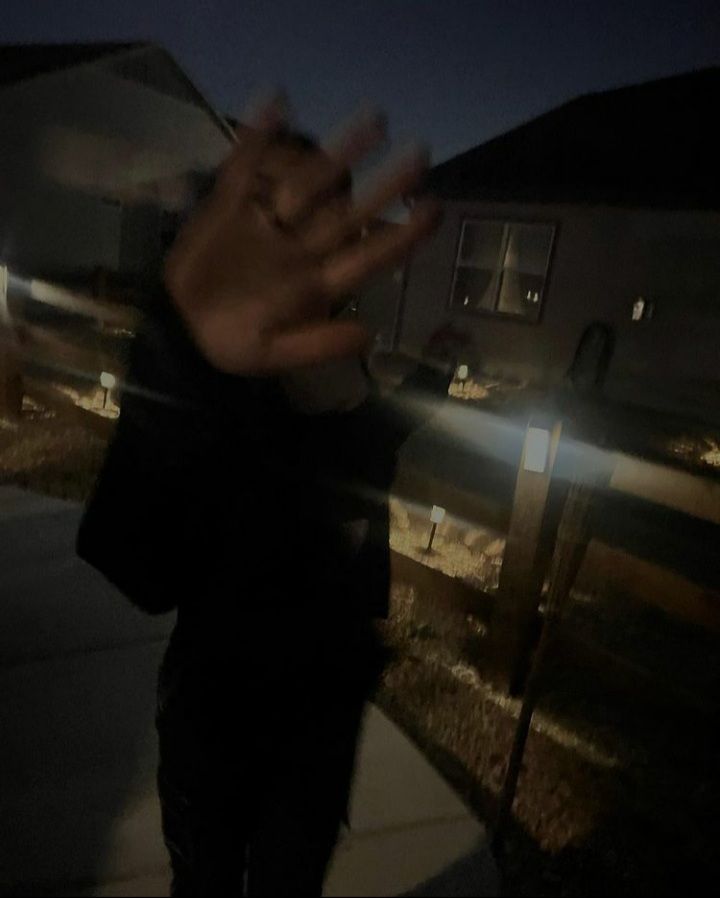 a person standing on a sidewalk with their hand up in the air and lights shining behind them