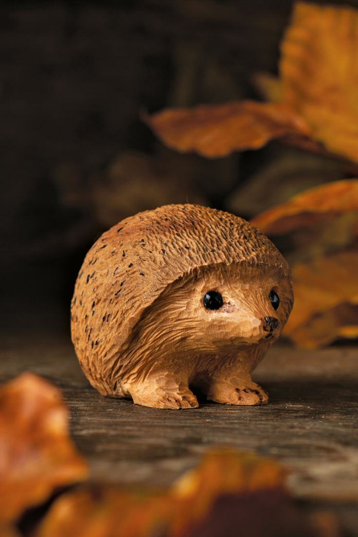 a hedgehog figurine sitting on the ground in front of some autumn leaves