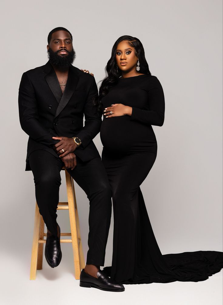 a pregnant couple sitting on a stool posing for the camera, with one man in a tuxedo and the other woman in a black dress