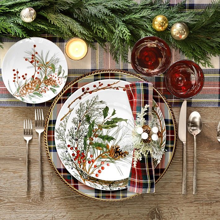 a place setting with plaid table cloth, silverware and evergreen branches on the plate