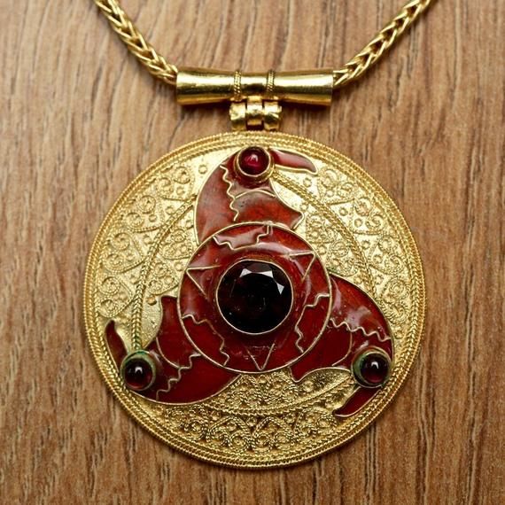 Replica of 7th century Triskelion pendant at the British Museum. Three whirling arms of cloisonné form bird heads decorated with cabochon eyes of deep-red garnet. Handmade of 24k gold vermeil and a large faceted garnet centerstone, this anglo-saxon pendant reproduction is sure to turn heads. Includes 14" braided chain. Pendant size: 1 3/4 inches. Byzantine Cabochon Jewelry For Gifts, Byzantine Jewelry With Cabochon For Gifts, Byzantine Style Cabochon Jewelry For Gifts, Ornate Bronze Jewelry For Ceremonial Occasions, Byzantine Style Cabochon Jewelry Gift, Byzantine Gold Cabochon Jewelry, Gold Byzantine Jewelry With Cabochon, Ceremonial Hallmarked Bronze Jewelry, Ceremonial Antique Gold Pendant Jewelry