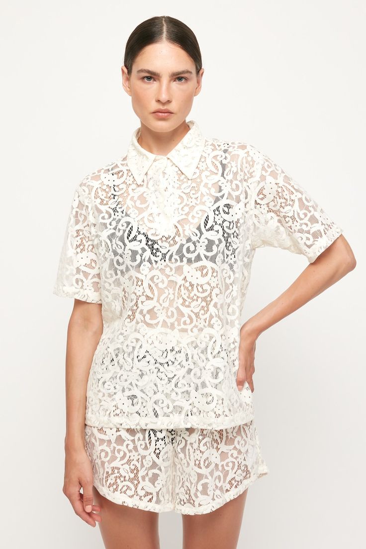 DESCRIPTION Flat Collar Shirt - USD 248.00 An S/W/F twist on the ¾ shirt, this feminine piece features a large, pointed collar that buttons down to the bust. The openwork lace finish in warm weather Ivory pairs particularly well with a contrasting black bralette. Wear yours with the matching short and an open toe sandal at your next ocean view lunch. Bralette not included. Color: First Impressions, Ivory Relaxed Short - USD 248.00 This tapered short cuts higher at the hip to elongate the legs as Collared Lace Tops For Summer, Collared Lace Blouse For Summer, Summer Collared Lace Tops, Summer Collared Lace Blouse, Summer Lace Collared Tops, Summer Lace Blouse With Collar, Collared Lace Blouse With Lace Top, Luxury Short Sleeve Blouse With Lace Collar, Lace Collared Top For Daywear