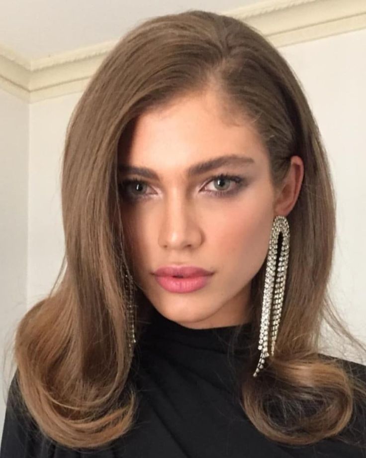 a woman with long brown hair wearing large silver earrings and black top looking at the camera