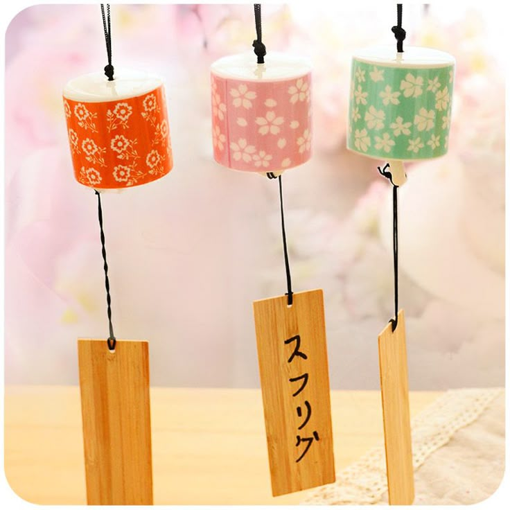 three tea cups are hanging from small wooden tags with japanese writing on them and flowers in the background