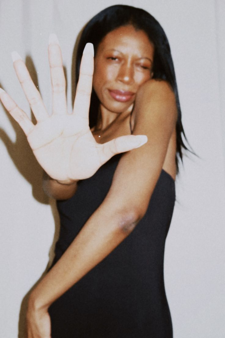 a woman in a black dress holding her hand up to the camera with both hands