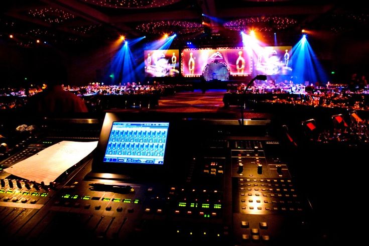 an electronic mixing console in front of a stage with lights and sound equipment on it