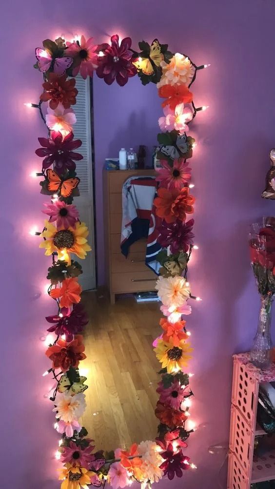 a mirror that has flowers on it and lights around the frame in front of it