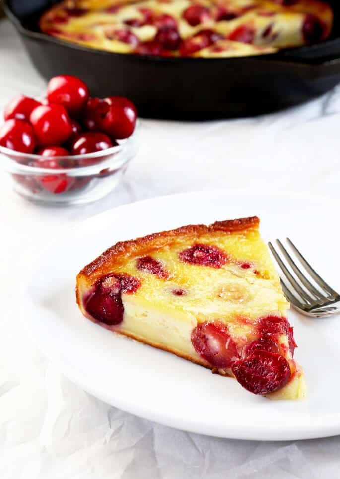 a piece of cake on a plate next to a bowl of cherries