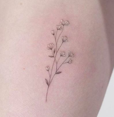 a small flower tattoo on the back of a woman's thigh, with tiny white flowers