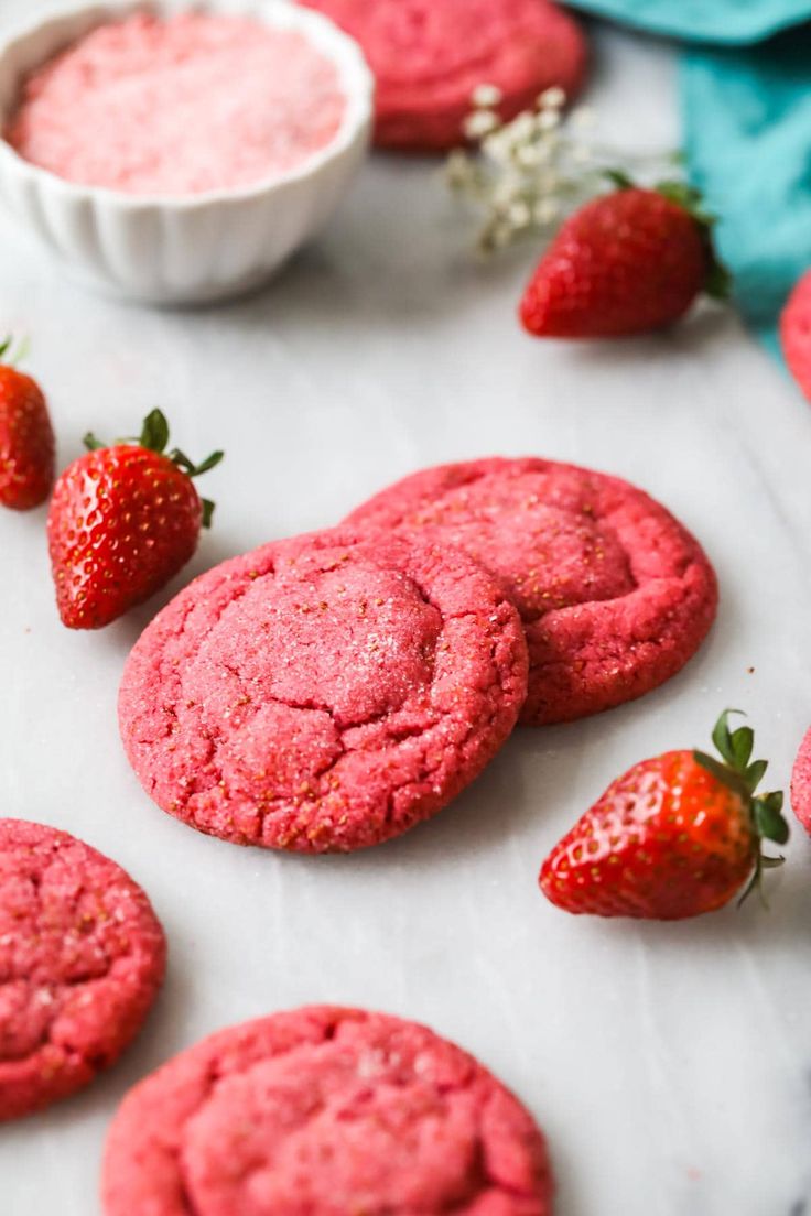 a woman holding a heart shaped cookie in front of some strawberry cookies