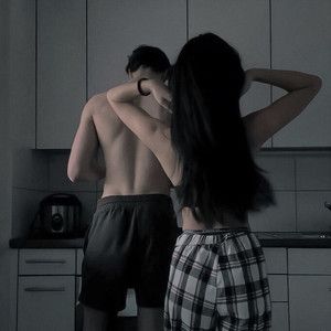 two people standing in the kitchen with their backs to each other and one person touching his hair