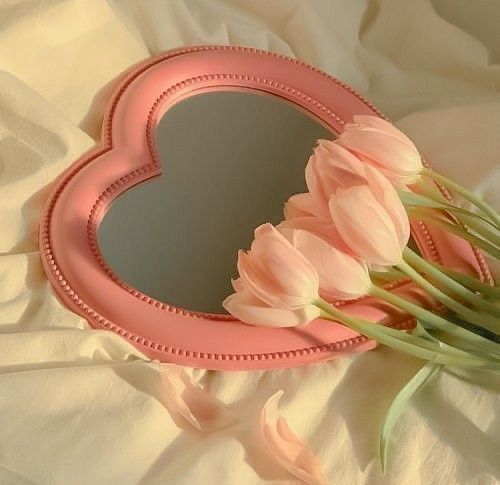 pink tulips in front of a heart shaped mirror on a white bed sheet