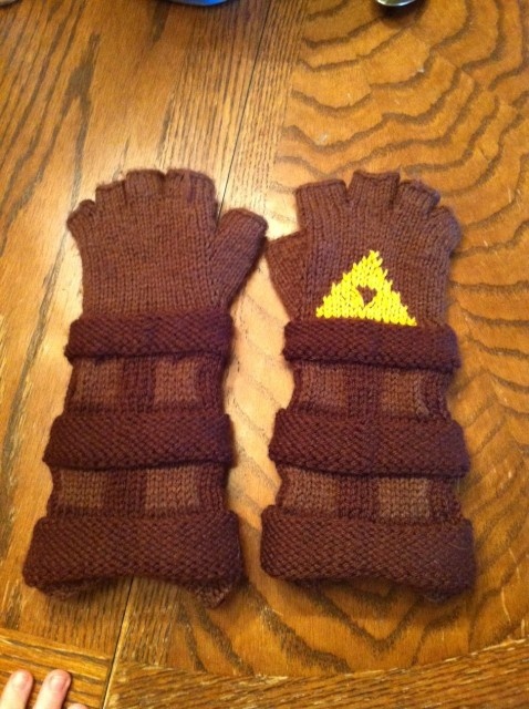 two brown mittens sitting on top of a wooden table next to a person's hand