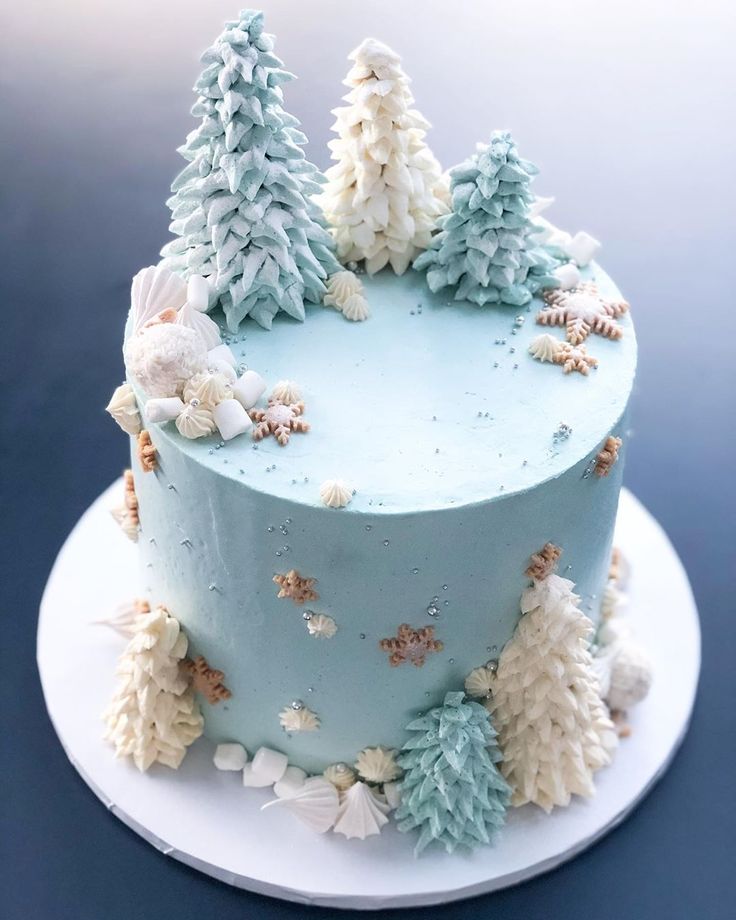 a blue frosted cake decorated with trees and snowflakes