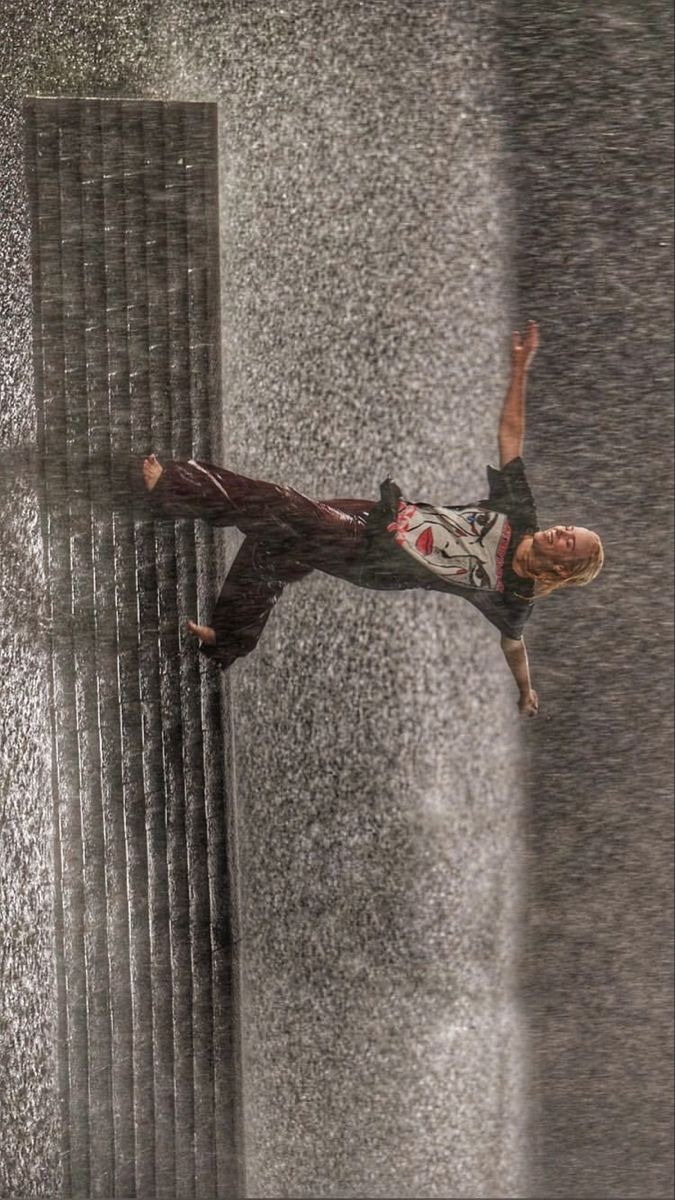 a man falling off his skateboard in the rain with water spraying up behind him