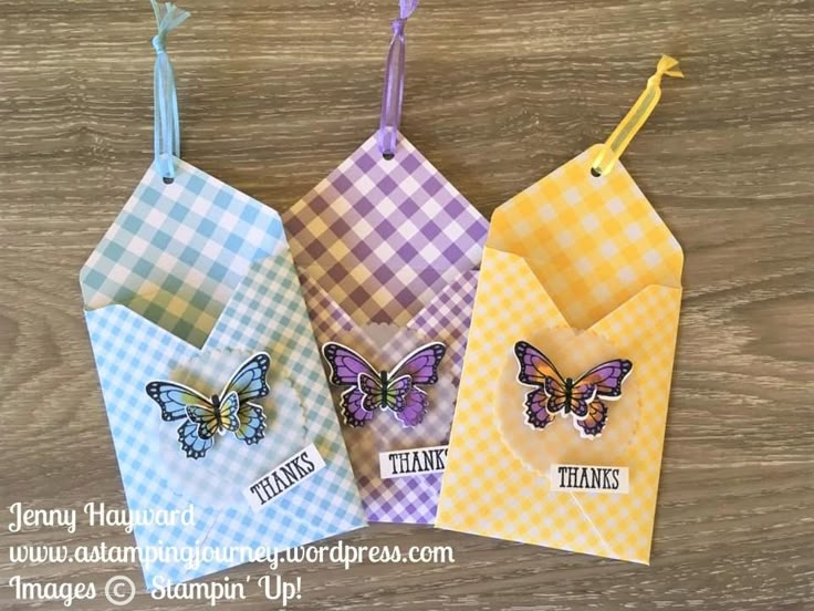 three tags with butterflies hanging from them on a wooden surface, one is yellow and the other is blue