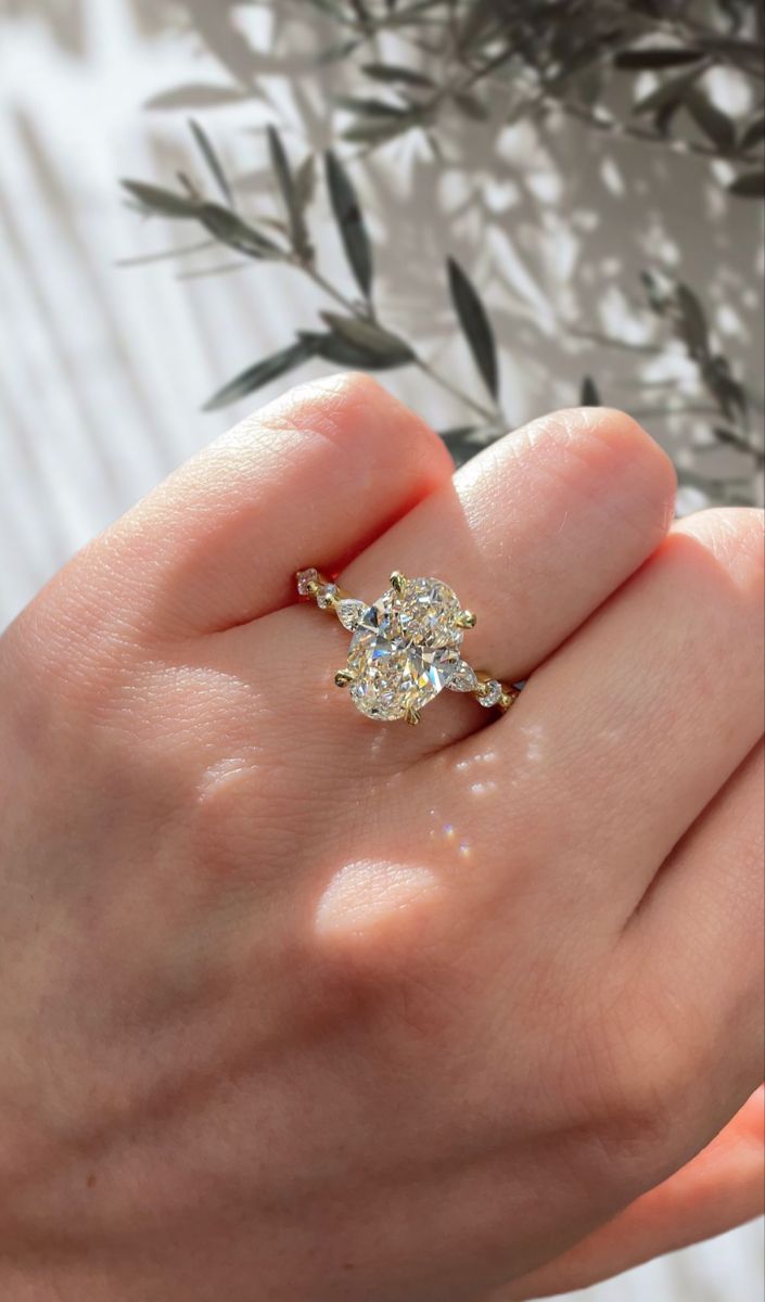 a woman's hand holding an engagement ring with two stones on it and leaves in the background