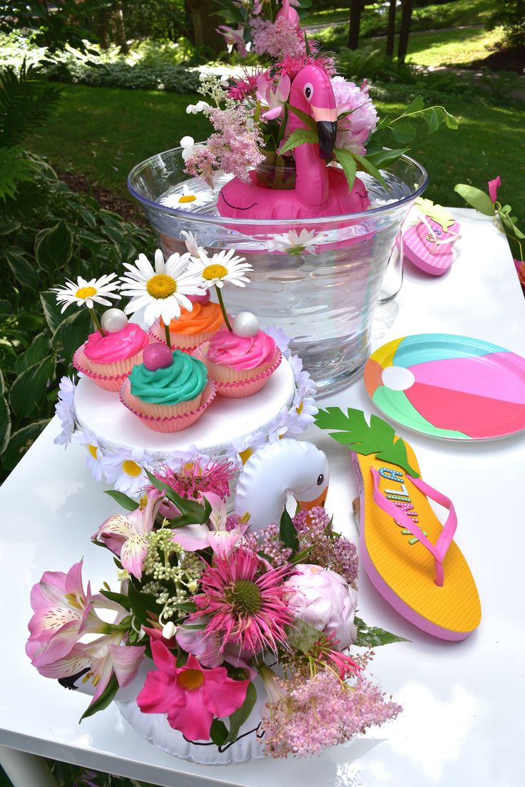 a table topped with cupcakes and flowers on top of a white table cloth