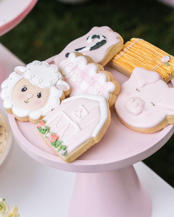 some cookies are sitting on a pink cake platter with farm animals and sheeps