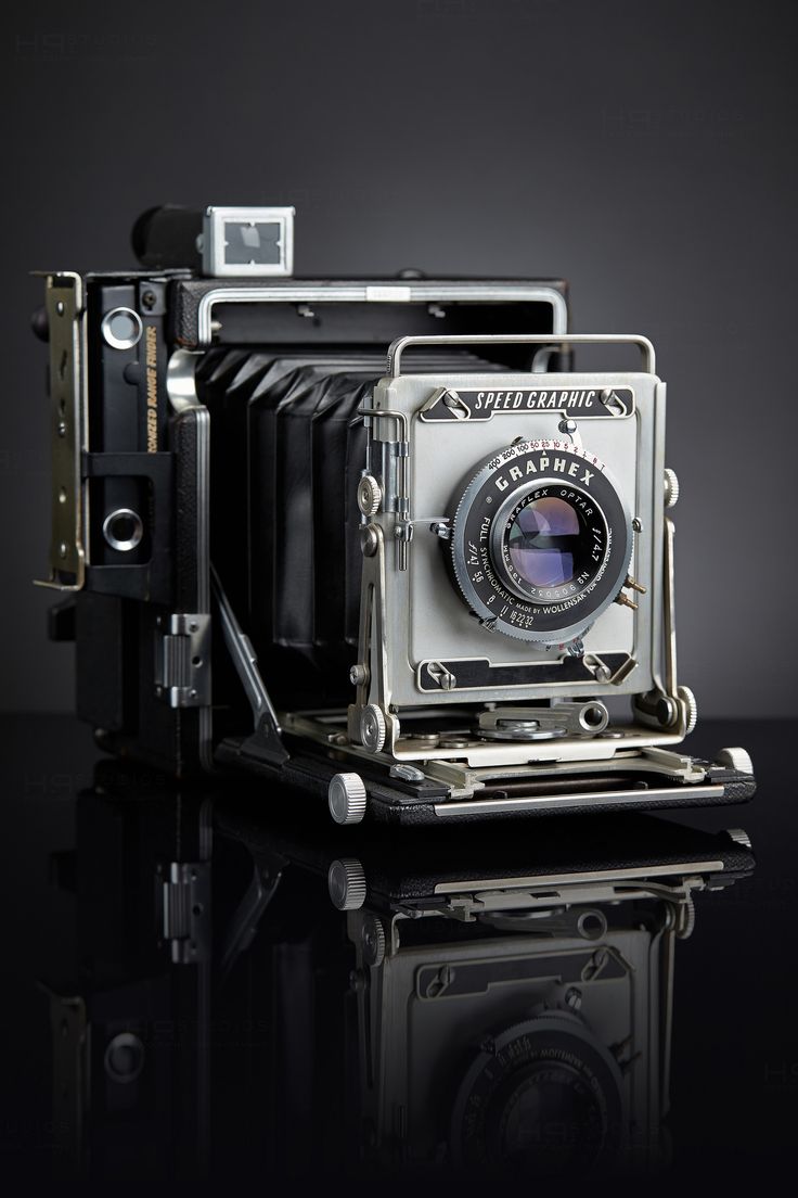 an old fashioned camera sitting on top of a black table next to a glass surface