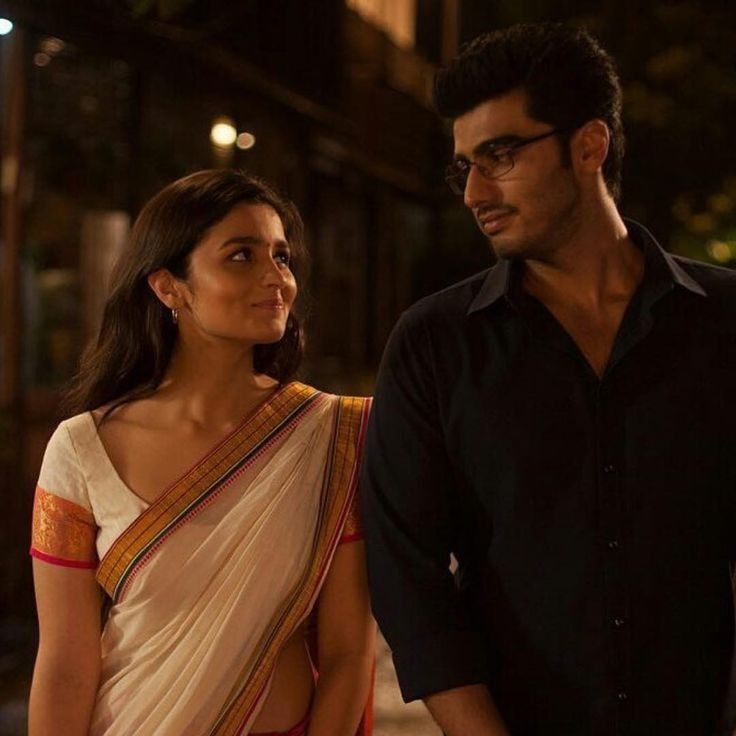 a man standing next to a woman in a white sari on the street at night